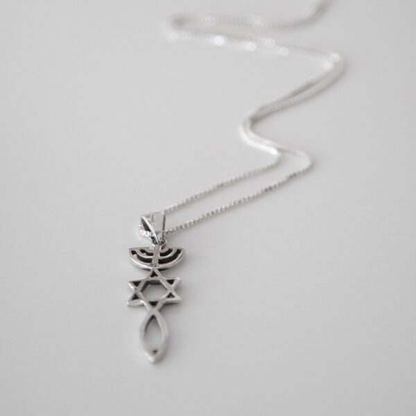 The One New Man Pendant necklace laying on a white table with the chain out of focus.